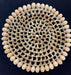 Circular placemat with cream-colored cowrie shells arranged around the border and woven tan geometric lattice pattern filling the center on a dark background.