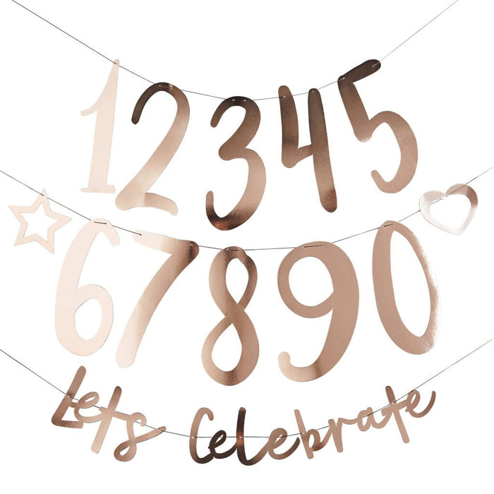 Rose gold metallic number banner featuring large digits 1, 2, 3, 4, 5, 6, 7, 8, 9, 0 with decorative stars and hearts, and "let's celebrate" text on strands.