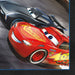 Two animated race cars, a red car with yellow flame design and a black car, shown on a napkin package with blue border detail.