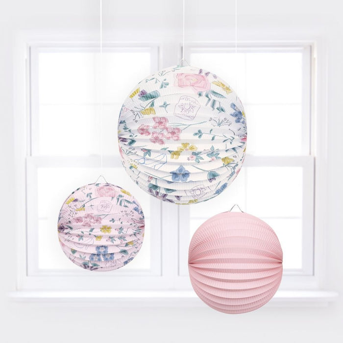 Disney Princess paper lanterns hanging in front of a window, featuring pink and floral designs for party décor.