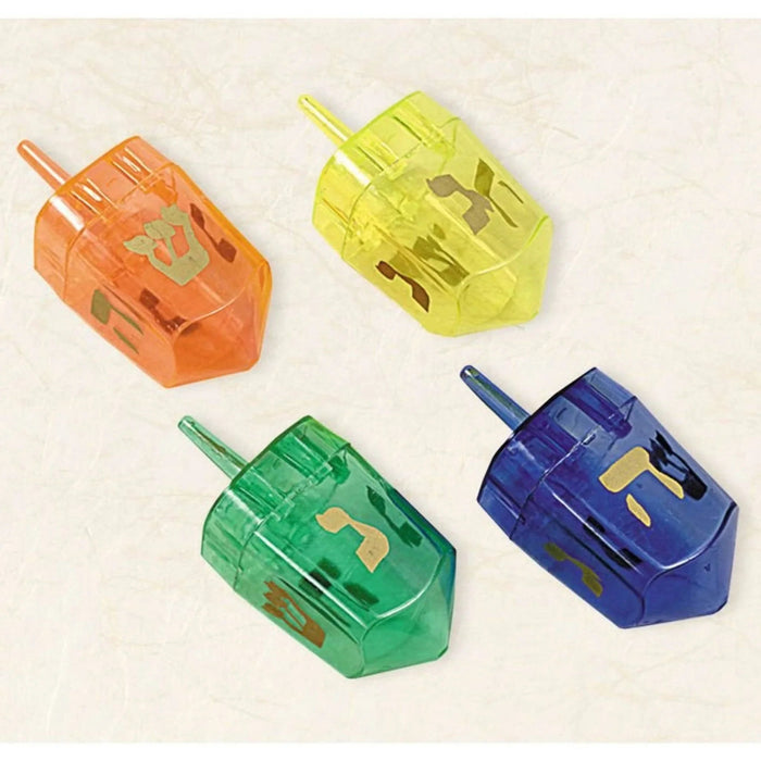 Four translucent plastic dreidels in orange, yellow, green, and blue with gold Hebrew letters displayed on a cream background.