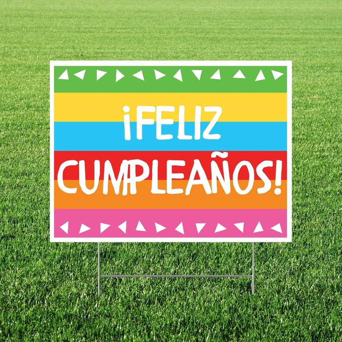 Colorful yard sign with horizontal stripes in green, yellow, blue, red, and orange displaying "¡FELIZ CUMPLEAÑOS!" in white text, decorated with white triangular bunting on top and bottom borders.