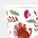 White cup featuring hand-painted autumn botanical illustrations in warm tones including a stylized turkey, pink and burgundy flowers, and brown leaf sprigs.