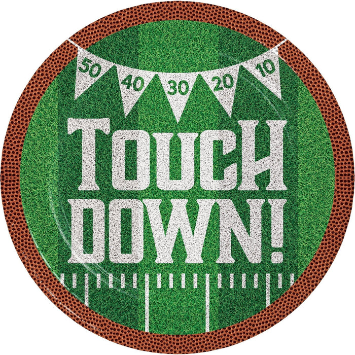 Round paper plate with brown football texture border, green grass field center, white "TOUCH DOWN!" text, yard line markings, and bunting banner with score numbers 50, 40, 30, 20, 10 displayed across top.