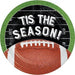Circular dessert plate with green grass-textured border, black center band with white "'TIS THE SEASON!" text, and brown football with white laces at the bottom.