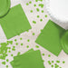 Bright lime green paper napkins and plates scattered on a white wooden surface with matching green confetti circles.