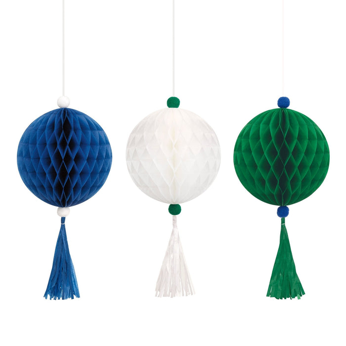 Three honeycomb ball decorations in blue, white, and green, each with matching tassel streamers and coordinating pom-pom toppers, suspended from strings.