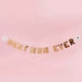 Gold "Best Mum Ever" banner with white daisy decorations strung on a pink background.