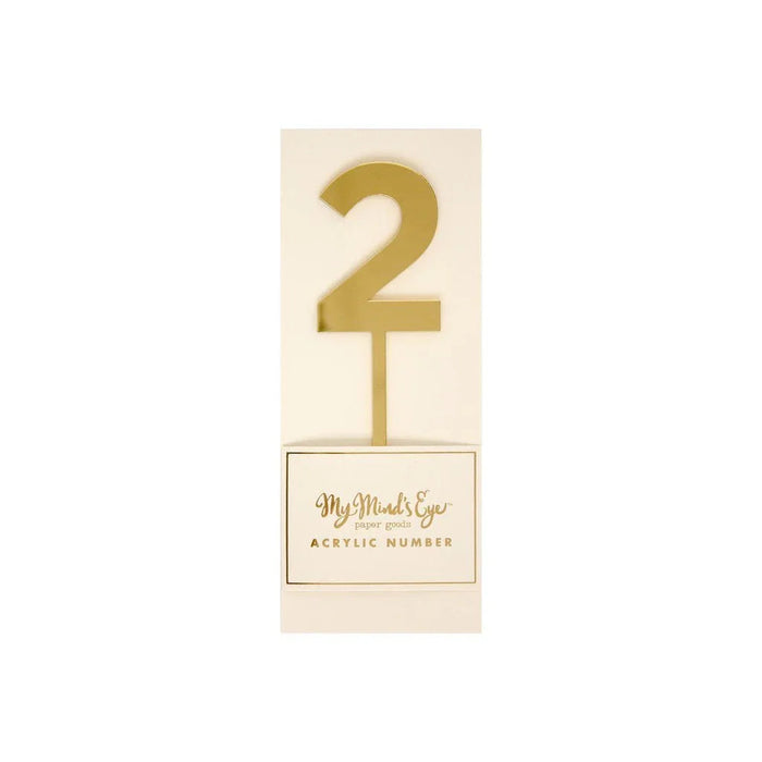 Gold number 2 acrylic cake topper with a stake base on cream-colored cardstock packaging labeled "My Mind's Eye paper goods acrylic number.