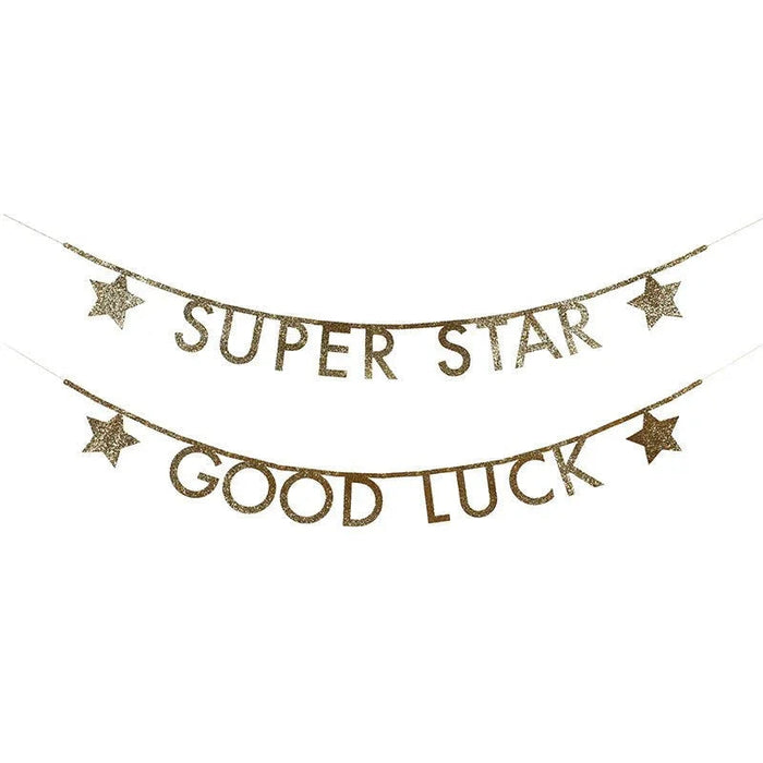 Two gold glitter letter banners with decorative stars strung on thin lines, reading "SUPER STAR" and "GOOD LUCK.