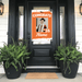 Graduation-themed poster on a black door with potted plants on either side.