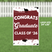 Burgundy and white yard sign with "CONGRATS Graduate CLASS OF '26" text, black graduation cap illustrations, and confetti design, measuring 24 by 36 inches.