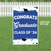 Blue yard sign with white text reading "CONGRATS Graduate CLASS OF '26" and graduation cap illustrations, measuring 24 inches by 36 inches.