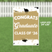 Large yard sign with tan and white design featuring "CONGRATS Graduate CLASS OF '26" text, graduation caps, and gold accents, measuring 24 by 36 inches.