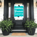 Turquoise and white graduation door banner reading "CONGRATS Graduate CLASS OF '26" with black mortarboard graphics, displayed on a black front door flanked by fern planters.