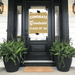 Gold and white door banner reading "Congrats Graduate Class of '26" with graduation cap graphics, displayed on a black front door flanked by fern planters.