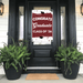 Burgundy and white graduation door banner reading "CONGRATS Graduate CLASS OF '26" displayed on a black front door with fern plants on either side.