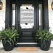 Silver and white "Congrats Graduate Class of '26" door banner displayed on a black front door with glass panels, flanked by two black planters with green ferns.