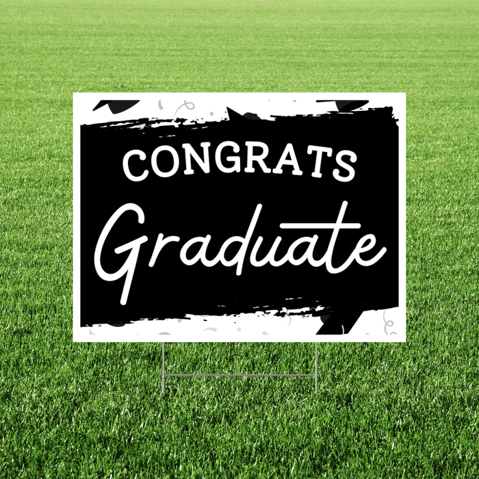 Black and white lawn yard sign with "CONGRATS" in bold capital letters and "Graduate" in white script font on a black brushstroke background, displayed on green grass.