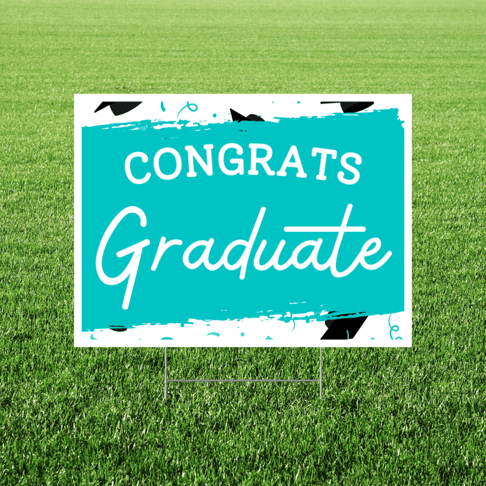 Turquoise and white yard sign with "CONGRATS Graduate" text in white lettering, decorated with black graduation cap illustrations and paint splatter accents.