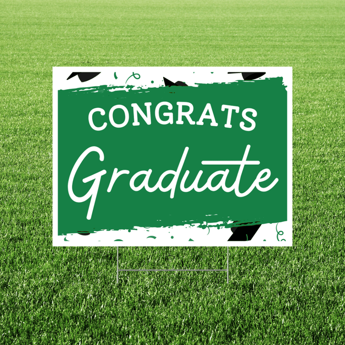 Green and white yard sign with "CONGRATS Graduate" text and graduation cap design, mounted on a stake in grass.