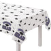 White plastic table cover with black graduation caps and diplomas scattered throughout, featuring purple "CONGRATS GRAD" text and banner designs along the edges.