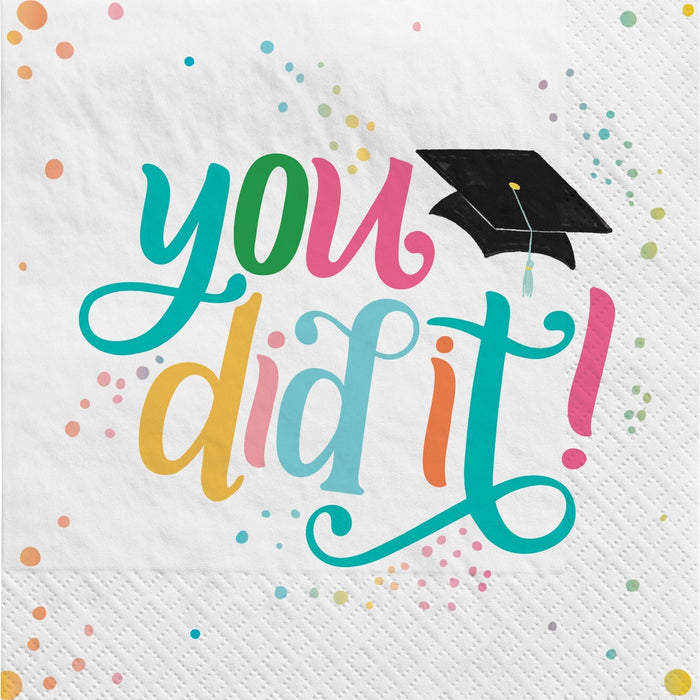 White paper napkins with colorful text reading "you did it" in teal, yellow, pink, and blue lettering, decorated with a black graduation cap and scattered pastel polka dots throughout.