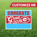 Red, white, and blue yard sign with "CONGRATS Grad 2026" text and a "G" logo, featuring metal stakes for outdoor display.