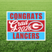 Yard sign with blue and red horizontal stripes reading "Congrats Grad 2026 Langers" with a large "G" logo in the center, displayed on grass.