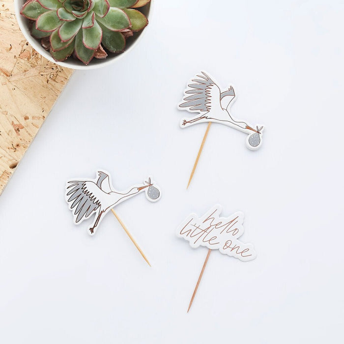 Three decorative food picks with wooden stems featuring stainless steel bird designs and "hello little one" text, displayed on white background with a potted succulent and cork coaster.