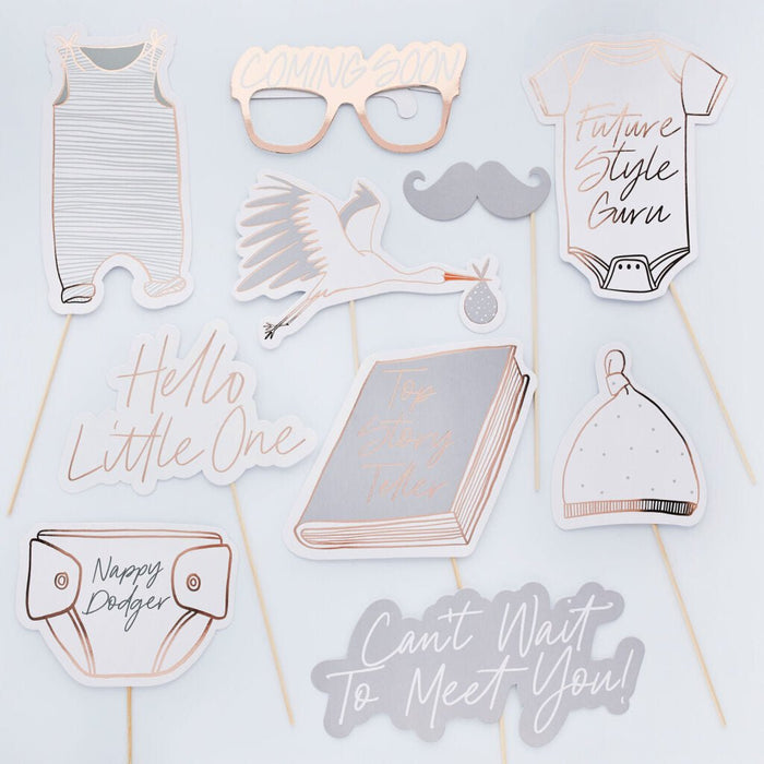 Ten rose gold and white baby shower photo booth props on sticks arranged on a light background, including onesies, glasses, mustache, book, bonnet, diaper, wings, and text phrases like "Hello Little One" and "Can't Wait to Meet You.