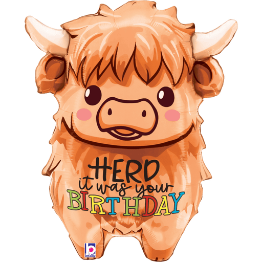 Orange mylar balloon shaped like a fluffy Highland cow with horns, brown eyes, pink cheeks, and text reading "it HERD it was your BIRTHDAY" in colorful letters across its body.