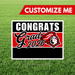Customizable yard sign with red and black horizontal stripes featuring "CONGRATS Grad 2026" text and a mascot logo, displayed on grass with a blank black section for personalization.