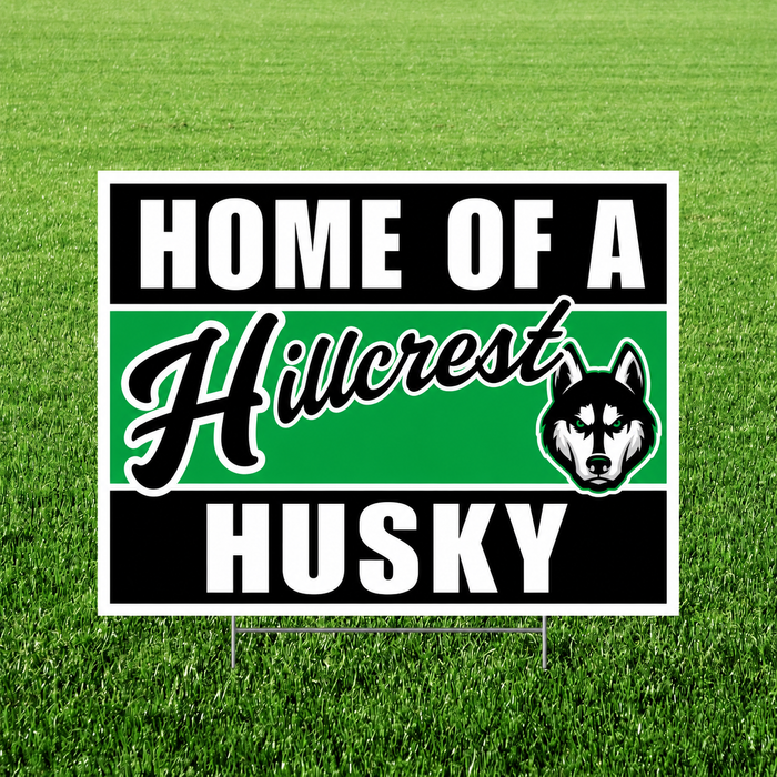 Hillcrest Huskies "Home of a Hillcrest Husky" graduation yard sign displayed on a green grass lawn. The square sign features bold black and white text with a green center stripe, the Hillcrest script logo, a husky mascot head with green eyes, and includes an H-stake for easy yard installation.