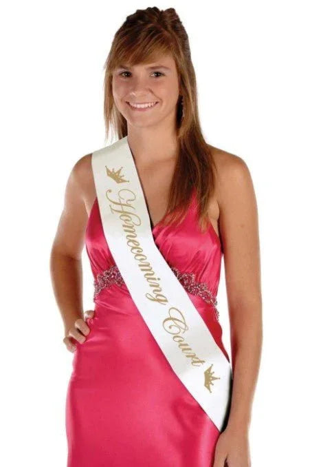 Young woman wearing a hot pink sleeveless dress with a white sash printed with gold text reading "Homecoming Court" and decorative crown designs.