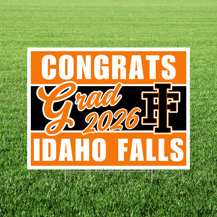 Orange and black yard sign with white text reading "Congrats Grad 2026 IF Idaho Falls" displayed on grass.