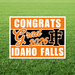 Orange and black yard sign with white text reading "Congrats Grad 2026 IF Idaho Falls" displayed on grass.