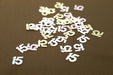 White and iridescent number 15 confetti pieces scattered on a tan surface, approximately 0.5 oz total.