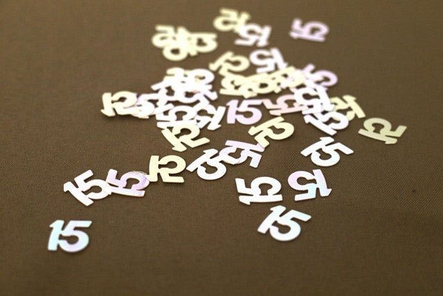 White and iridescent number 15 confetti pieces scattered on a tan surface, approximately 0.5 oz total.