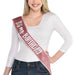 Smiling woman wearing a white long-sleeve top and jeans with a burgundy glitter sash diagonally across her body that reads "It's My Birthday" in white text.