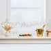 Wooden "Just Married" banner in natural beige script lettering hanging above an elegant white mantelpiece display with champagne, cupcakes, cake slices, pampas grass, and gold accents.