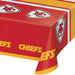 Red plastic table cover with Kansas City Chiefs arrowhead logos in white and gray, gold and red striped borders, and yellow "CHIEFS" text repeated along the edges.