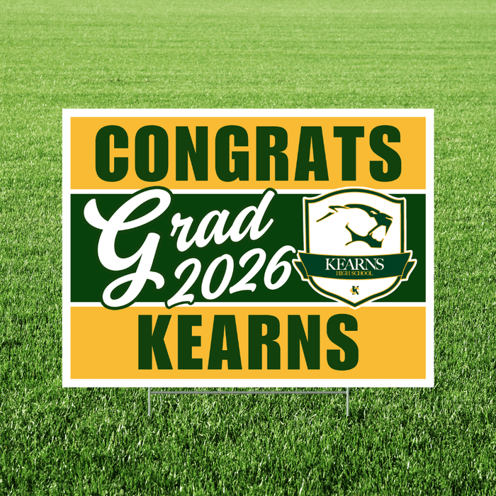 Yard sign displaying green and gold horizontal stripes with "CONGRATS Grad 2026 KEARNS" text and the Kearns High School logo on grass.