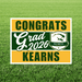 Yard sign displaying green and gold horizontal stripes with "CONGRATS Grad 2026 KEARNS" text and the Kearns High School logo on grass.