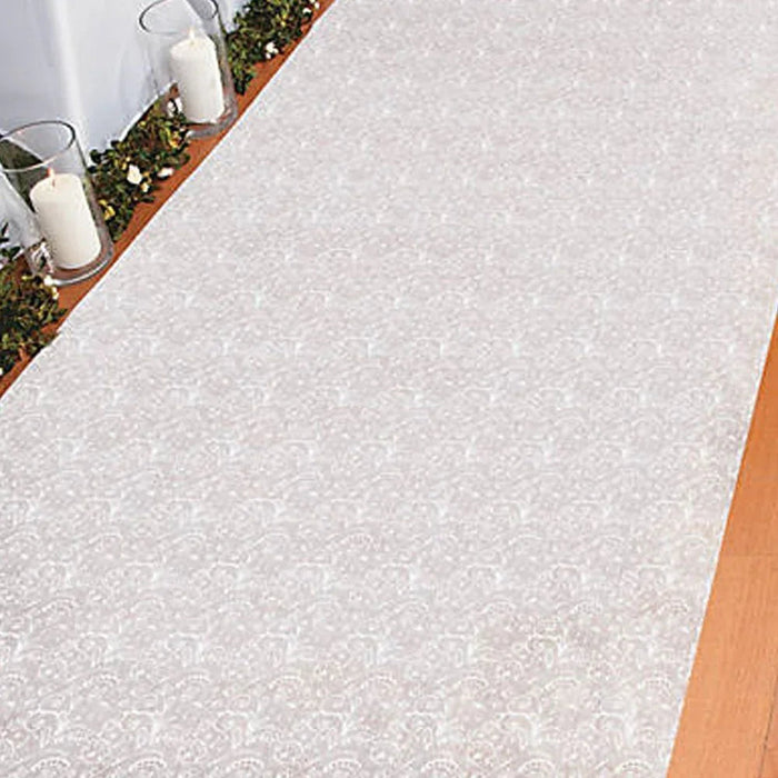 White lace patterned aisle runner displayed on wooden flooring with decorative greenery and white candles arranged along the top edge.