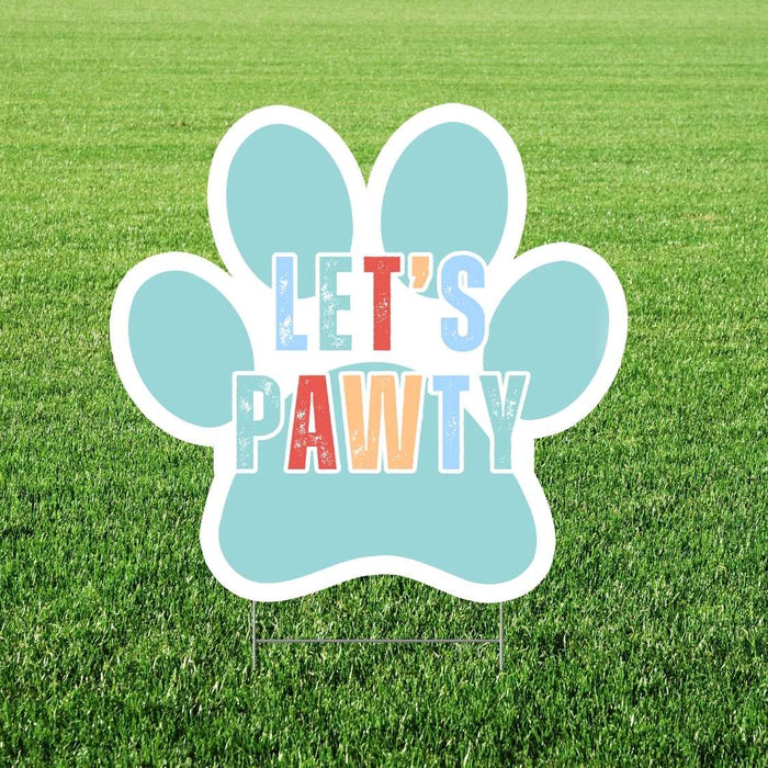 Turquoise paw print-shaped yard sign with white border displaying colorful text reading "Let's Pawty" in multicolored letters on green grass background.