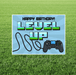 Gamer birthday yard sign featuring “Happy Birthday! Level Up” text in pixel-style lettering, a black game controller graphic, and a cord design on a light blue rectangular sign displayed in grass.