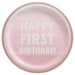 Pink round paper plate with white text reading "Happy First Birthday" and a tan ribbed border.