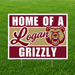 Logan Grizzlies "Home of a Logan Grizzly" graduation yard sign displayed on a green grass lawn. The square sign features bold crimson and white text with a gold center stripe, the Logan script logo, the official grizzly bear mascot, and includes an H-stake for easy yard installation.