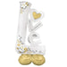 White and gold foil balloon shaped as the word "Love" with a yellow heart cutout, decorated with white flowers and gold leaf accents, standing on a gold base.